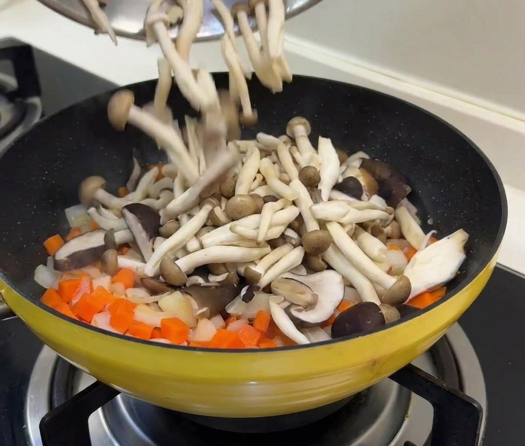 炒めた野菜の中にきのこと下ゆでしたグリーンピース、たけのこを加える様子。