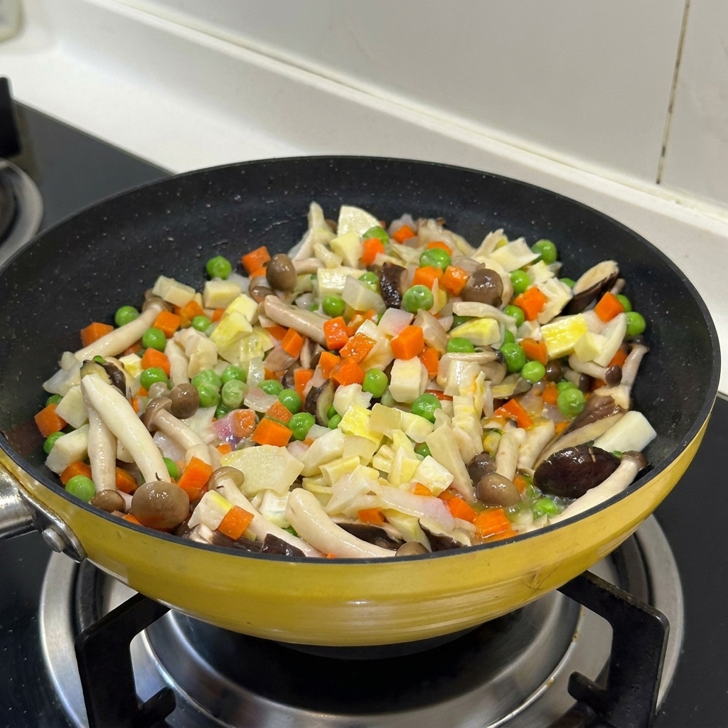 色とりどりの野菜ときのこがフライパンの中で混ざり合っている様子。