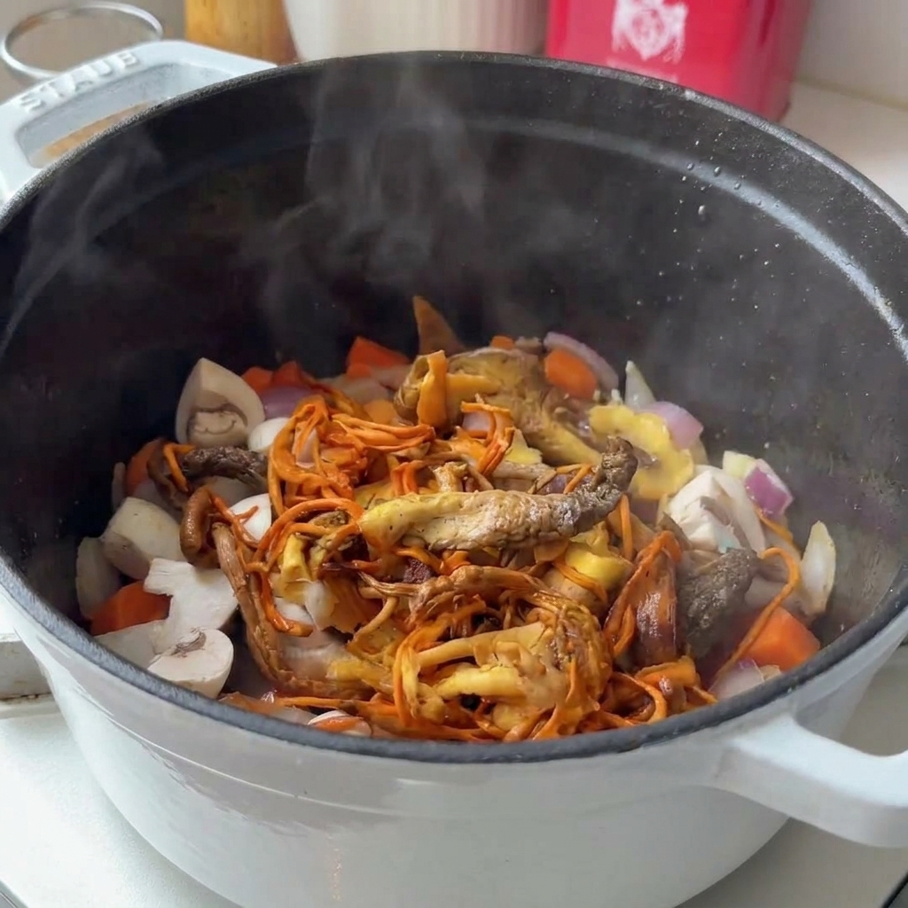 炒めた野菜の入った鍋にスライスしたキノコを加えている様子。
