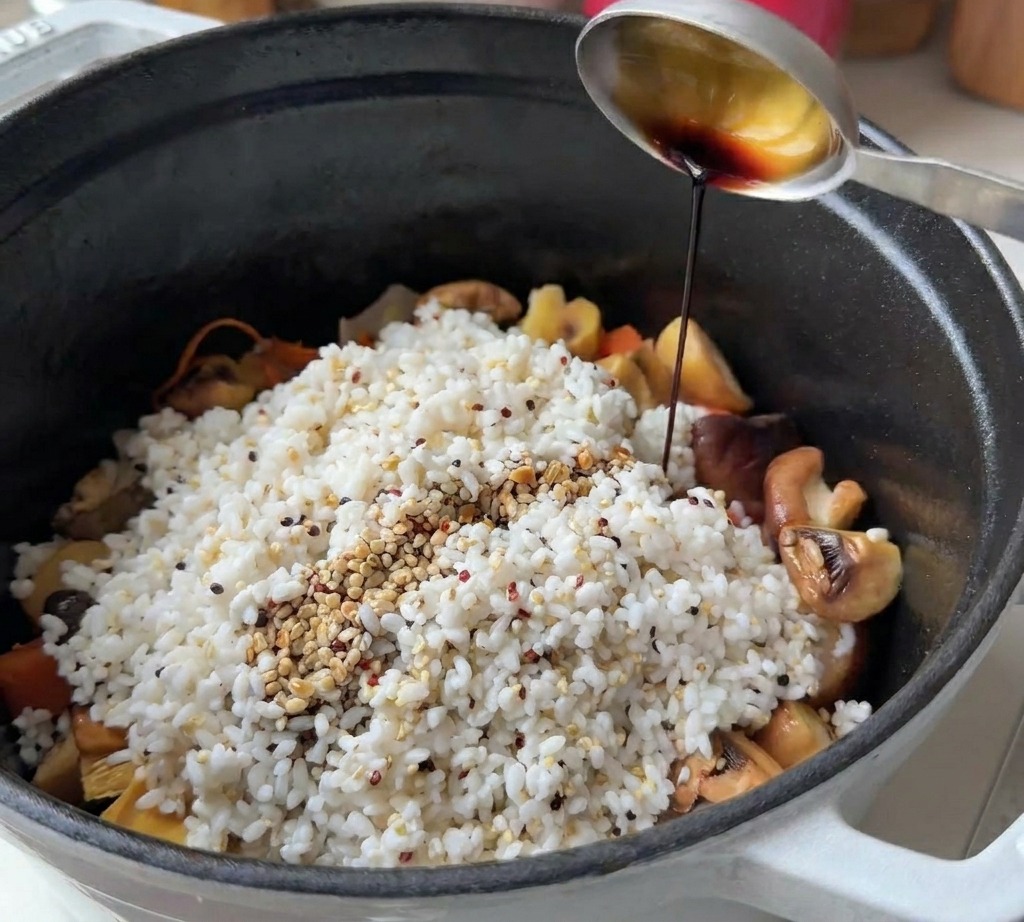 鍋の中の米と具材に醤油を回しかけて味付けしている様子。