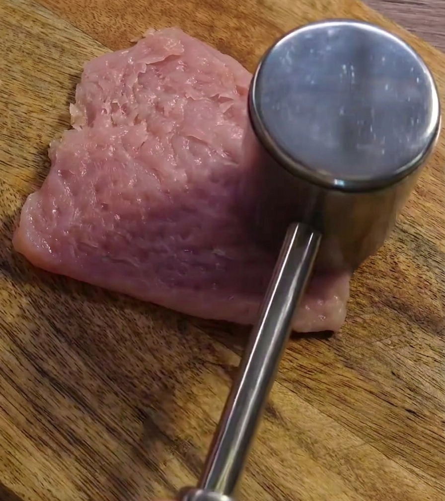 ミートハンマーで豚肉を平らに叩いている様子