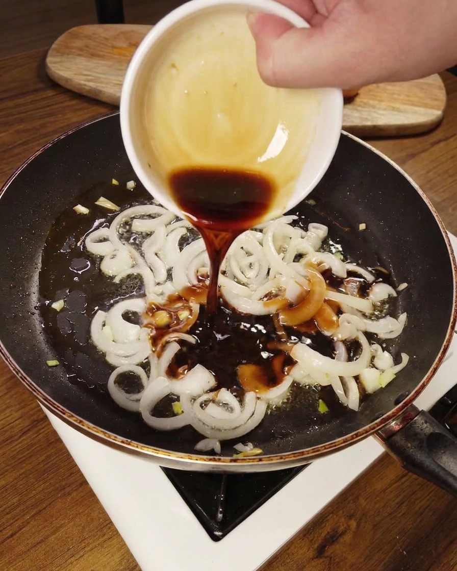 炒めた玉ねぎにタレをかけている様子
