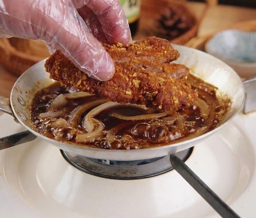 煮立った玉ねぎの上にトンカツをそっと置いている様子