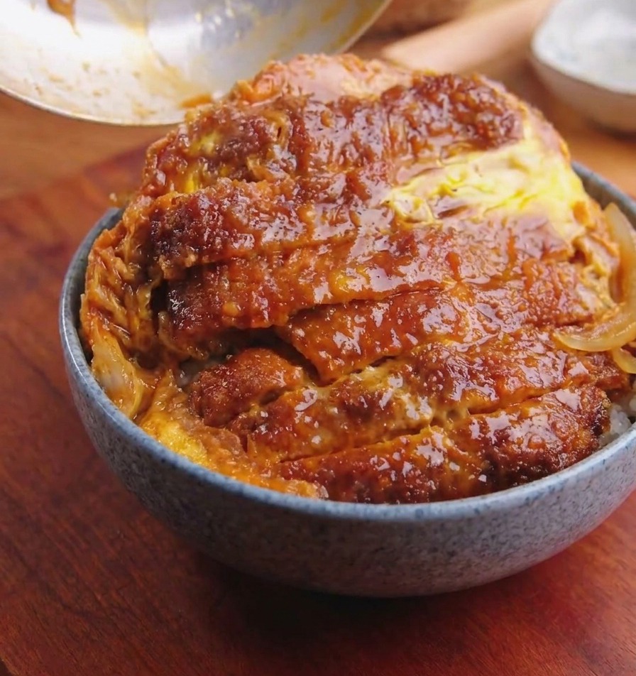 鍋からカツと卵を滑らせてご飯の上に乗せている様子