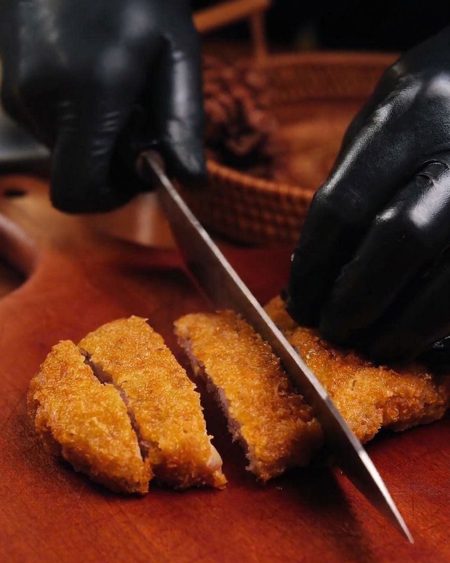 まな板の上で、揚げたてのトンカツを包丁で細長く切り分けている様子。