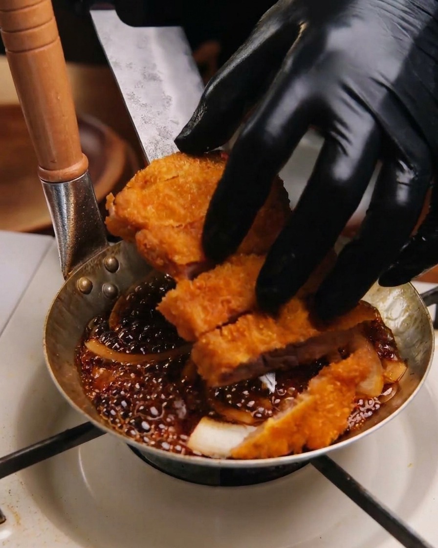煮立っている玉ねぎの上に、切り分けたトンカツを並べている様子。