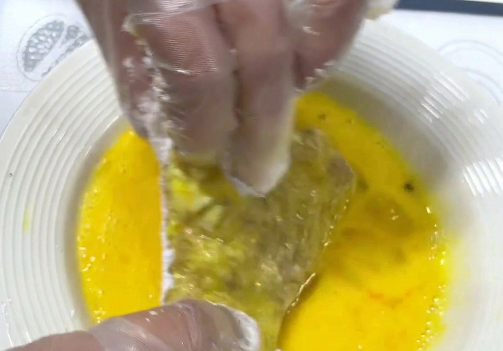 粉をつけた肉を黄金色の溶き卵にたっぷりと浸している様子