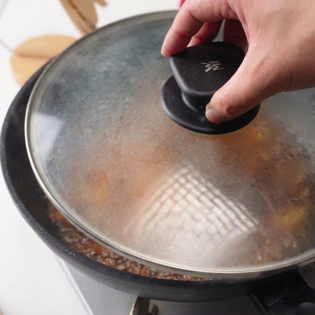鶏肉とタレが入ったフライパンに、透明なガラスの蓋を被せている様子。