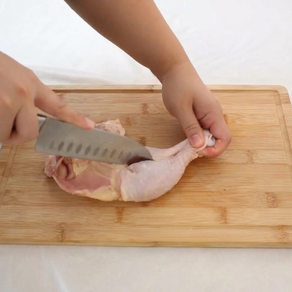 まな板の上で包丁を使い、鶏もも肉から慎重に骨を切り離す様子。