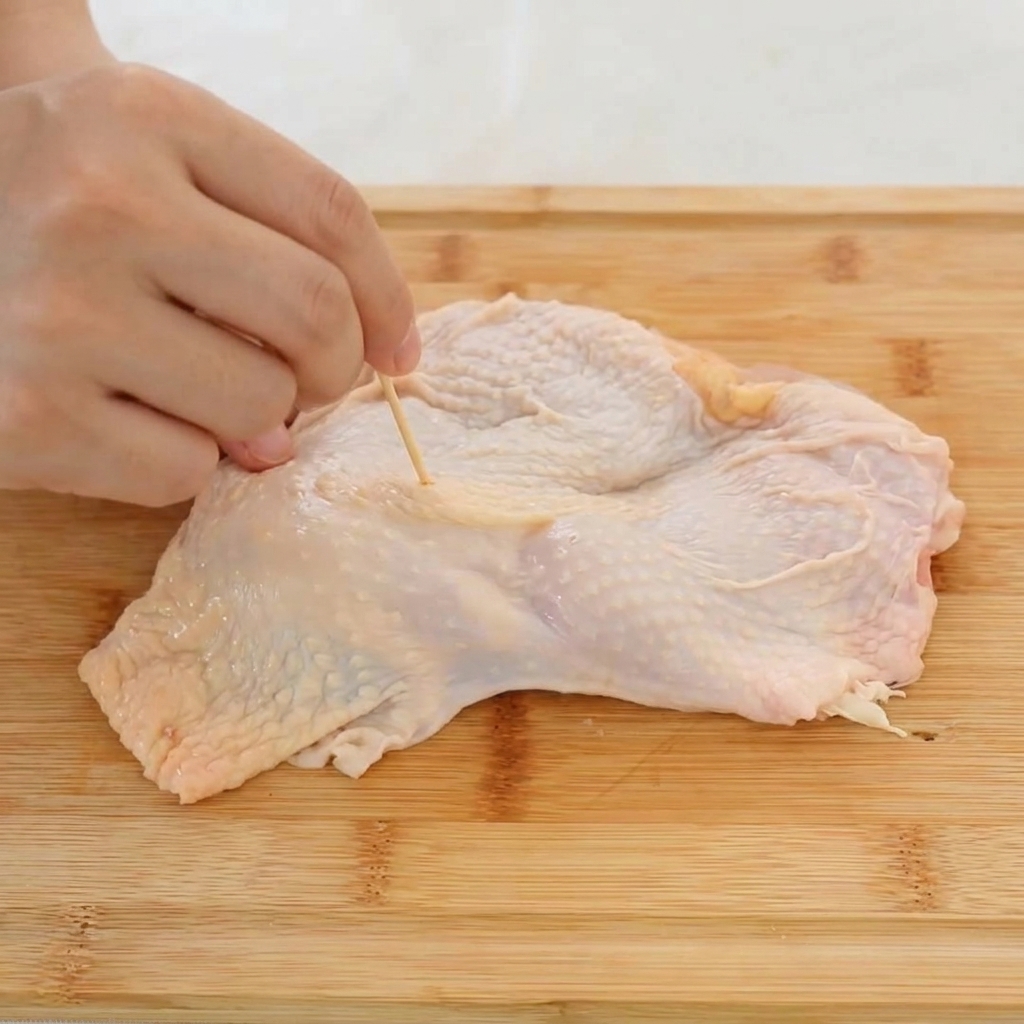 爪楊枝を使って鶏もも肉の皮全体に穴を開けている様子。