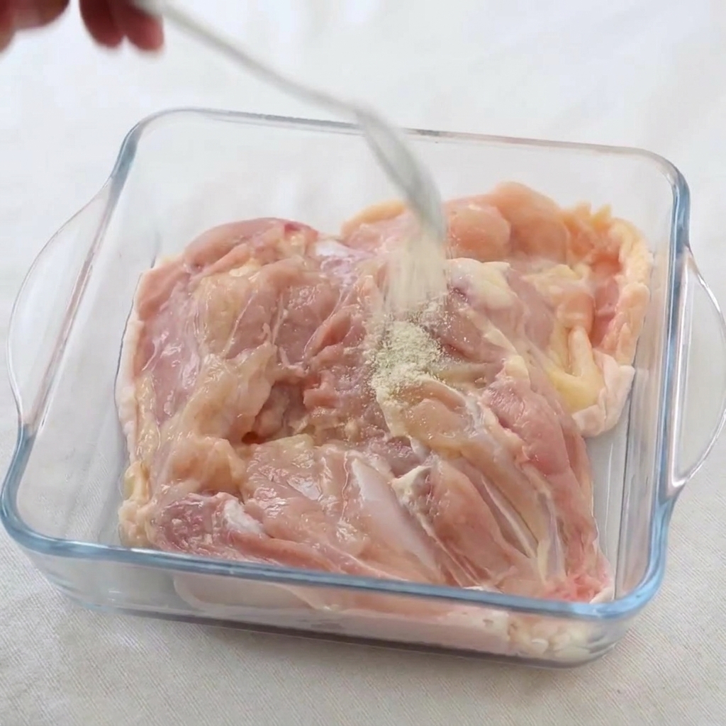 ガラス容器に入った鶏肉に、白胡椒と塩を振りかけている様子。