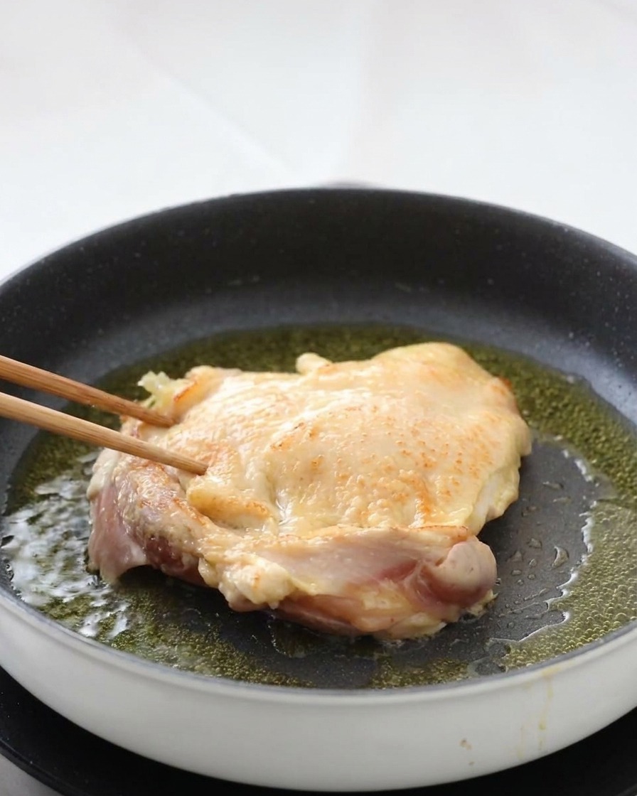 菜箸で鶏肉を裏返し、こんがりと焼けた皮目が見えている様子。