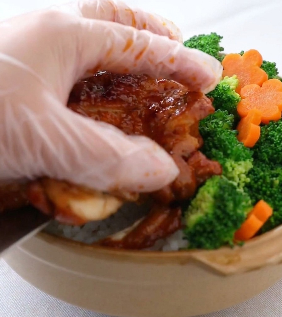 ご飯の上に鶏肉を乗せ、ブロッコリーと花形の人参を添えている様子。