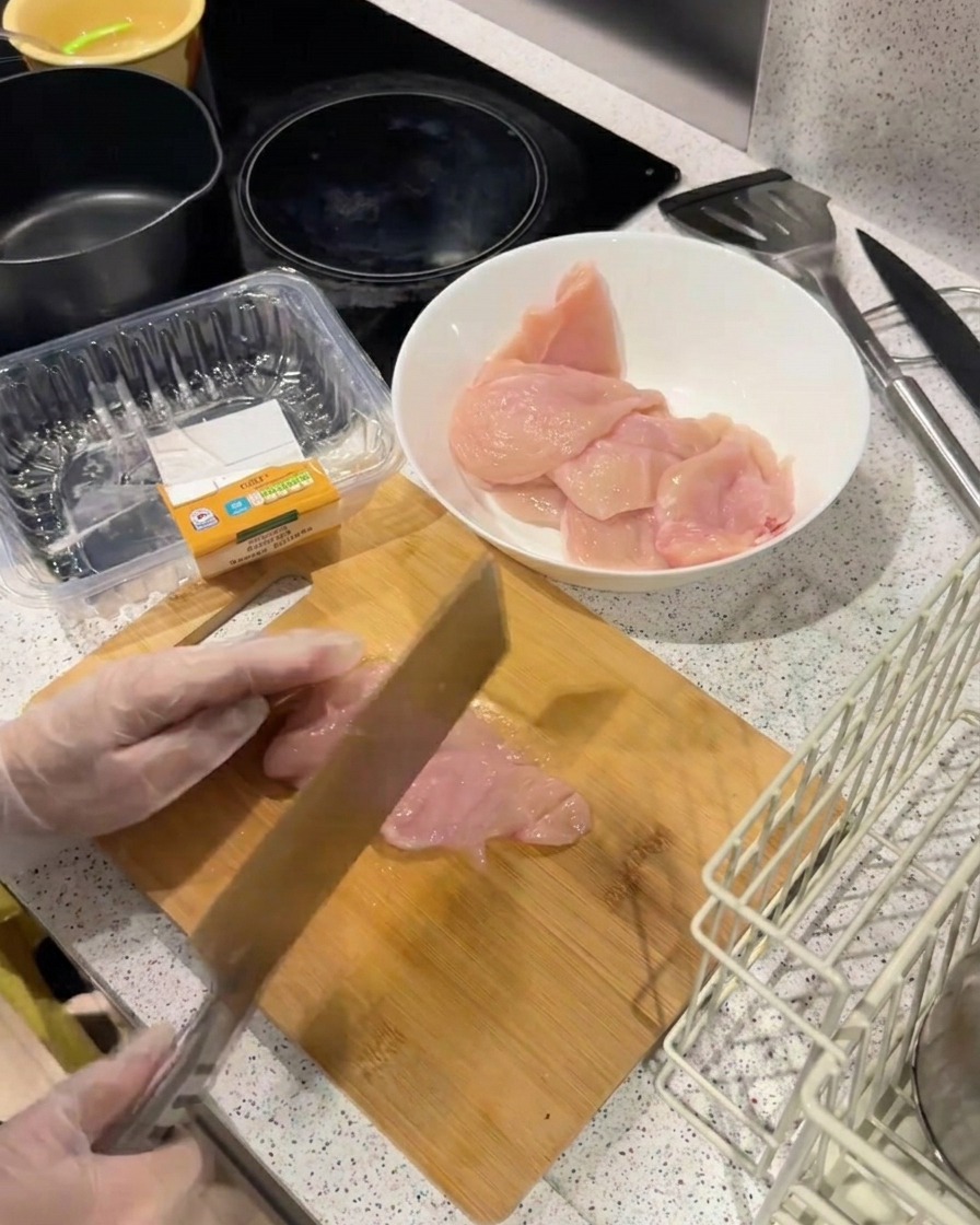 まな板の上で、包丁の背を使って鶏むね肉を叩いて平らにし、柔らかくしている様子