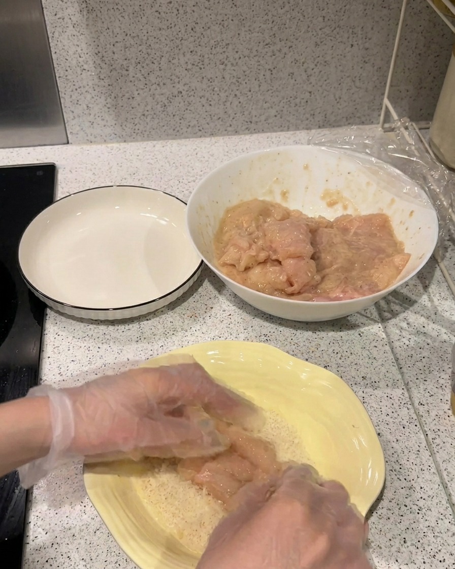 下味をつけた鶏肉を、パン粉がたっぷり入った黄色い平皿に押し当てている様子