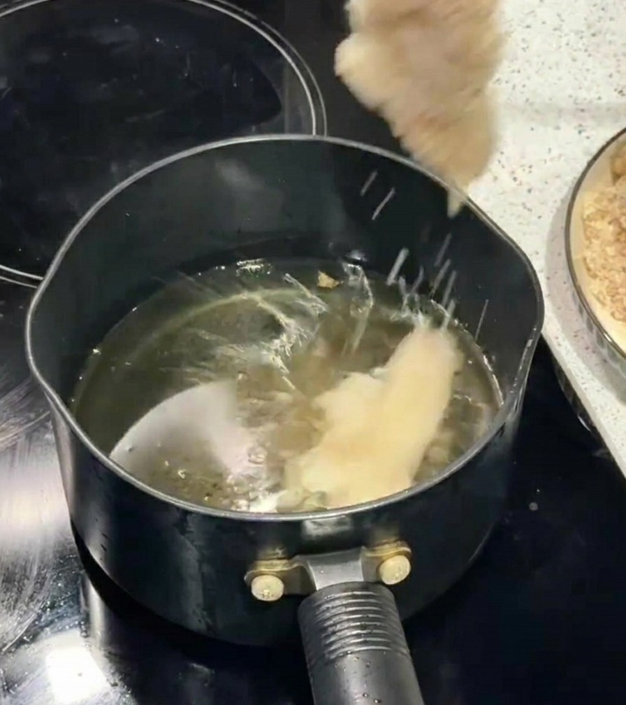パン粉をつけた鶏肉を、菜箸を使って熱した油の中へ静かに入れている様子