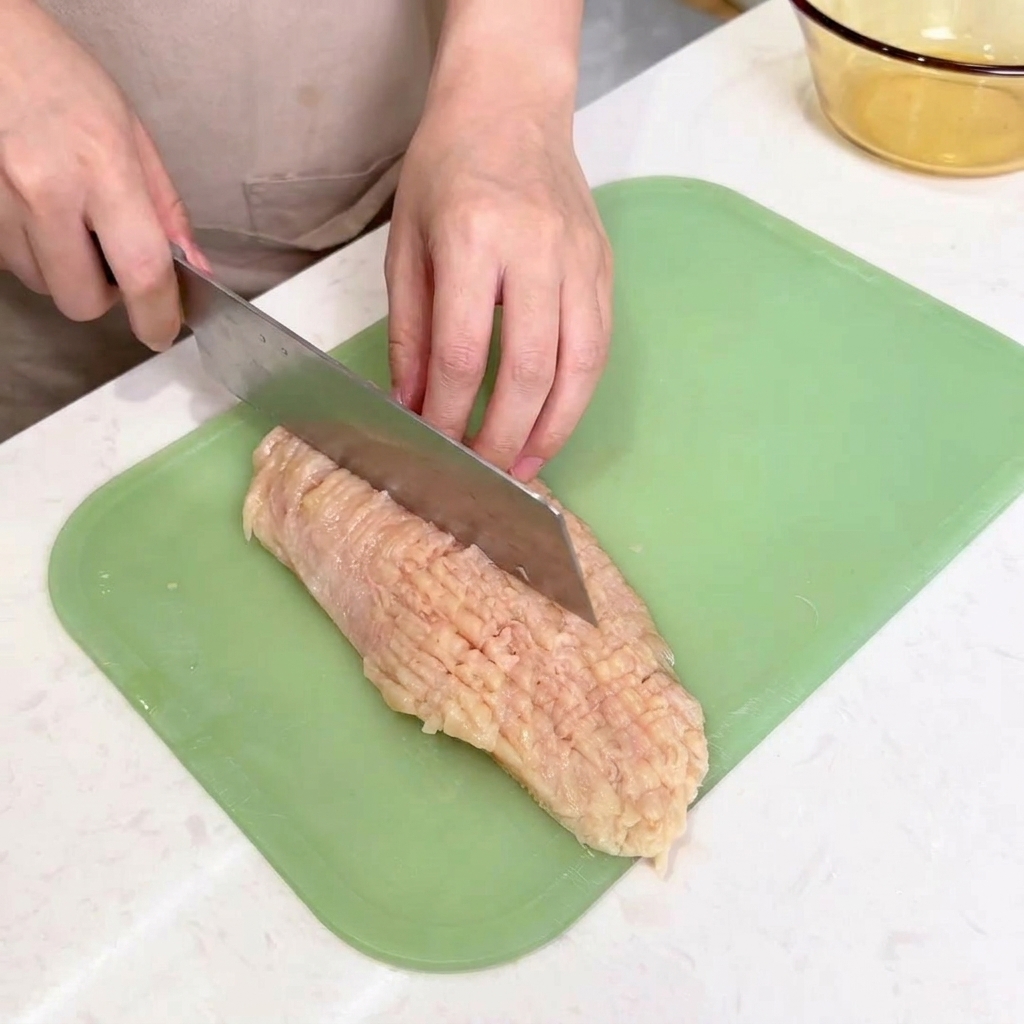 包丁の背を使って、まな板の上の鶏肉を軽く叩いて伸ばしている様子。