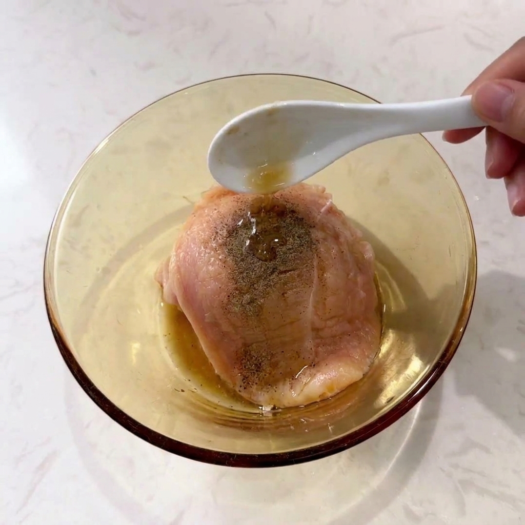 ボウルに入れた鶏肉に、スプーンで調味料を振りかけている様子。