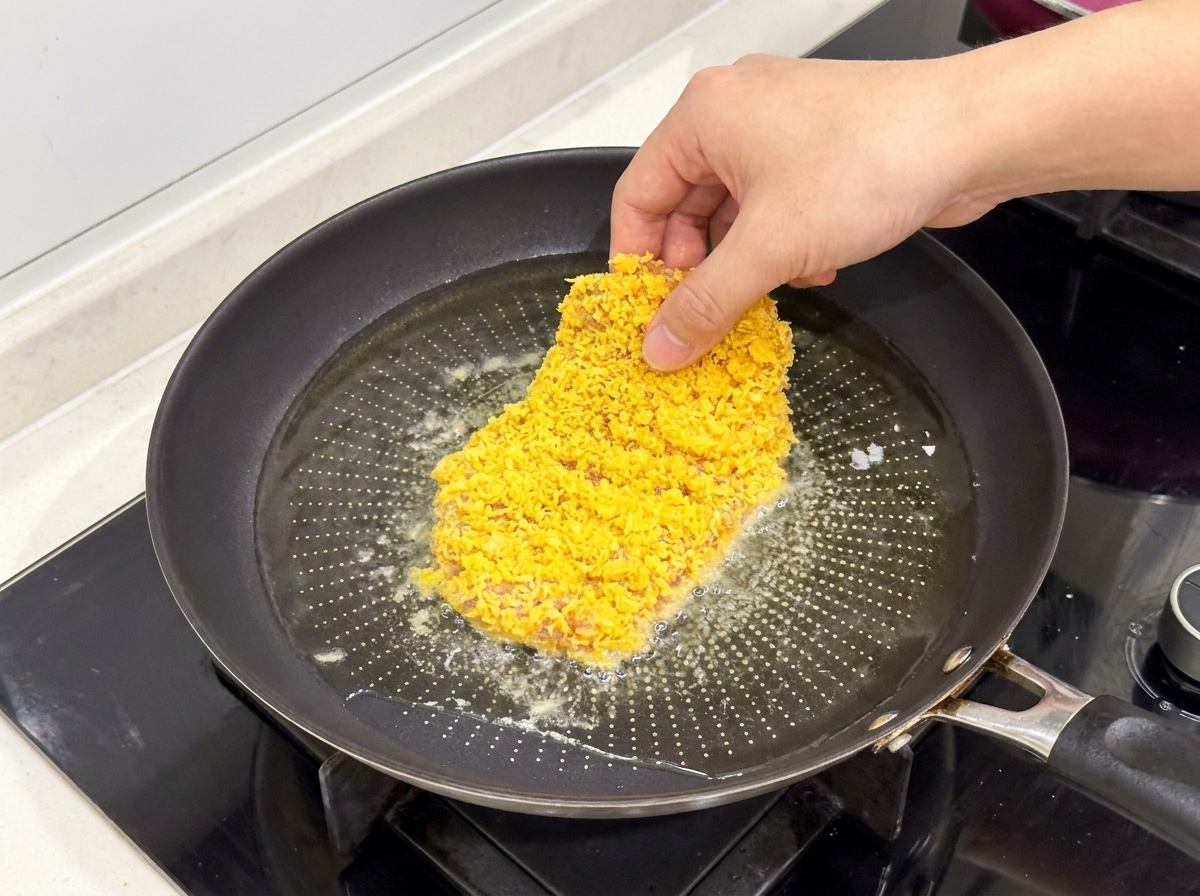熱した油の入ったフライパンに、衣をつけたチキンカツを入れている様子。