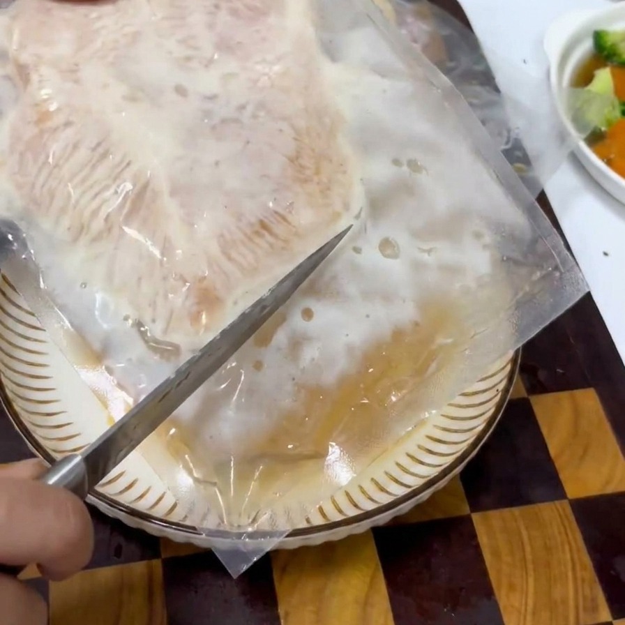 真空パックに入った味付け済みの鶏肉を包丁で開封している様子。