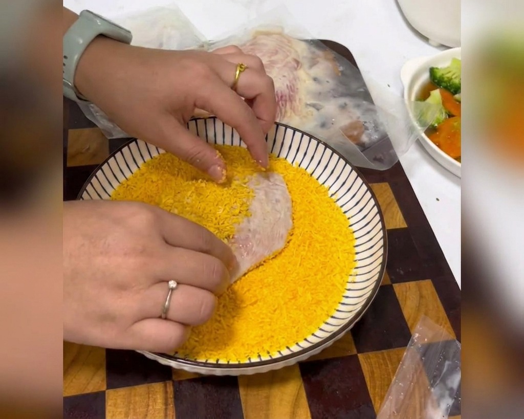 鶏肉をパン粉が入った容器に入れ、手でしっかり押し当てて衣をつけている様子。