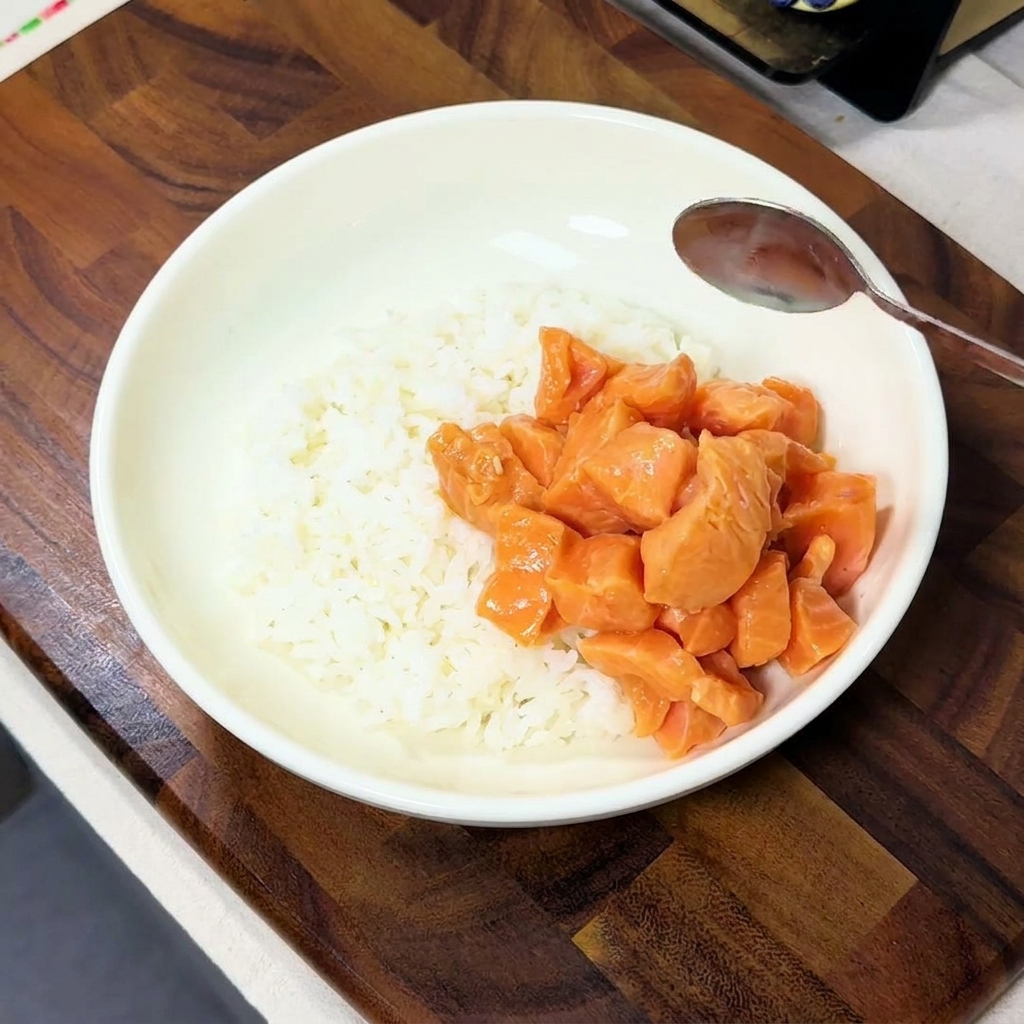 白い丼に盛られたご飯の上に、漬け込んだサーモンを盛り付けている様子