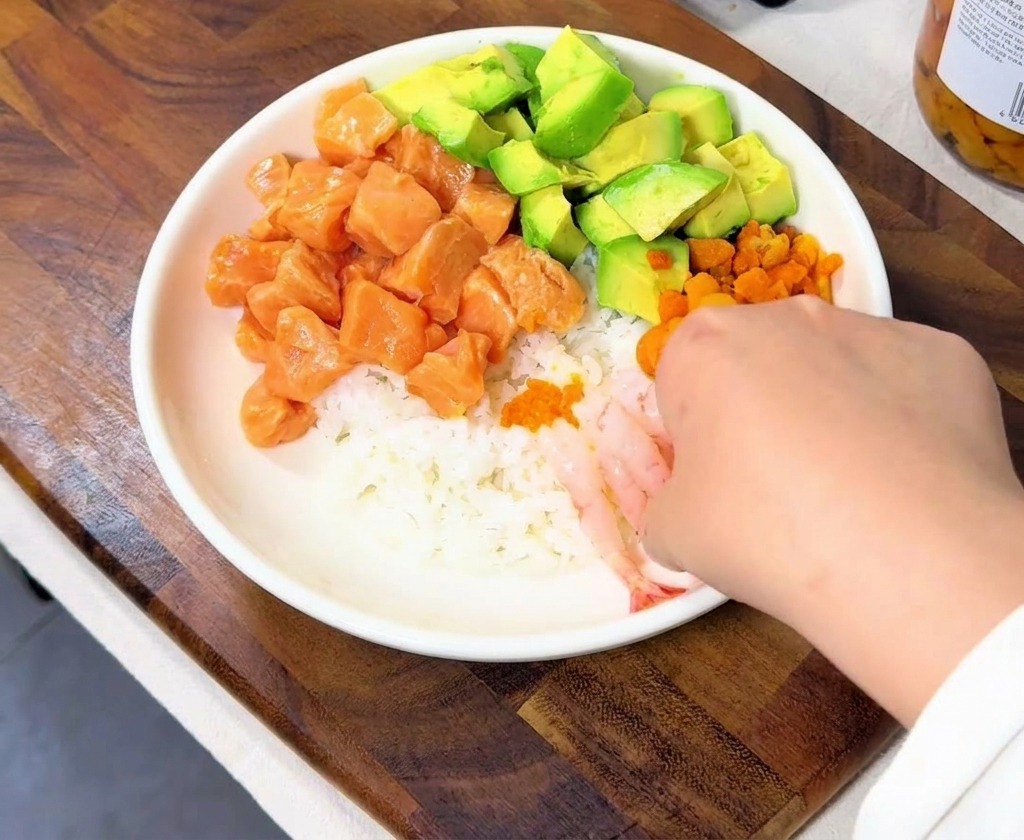 丼の端に、透き通ったピンク色の甘エビを並べている様子