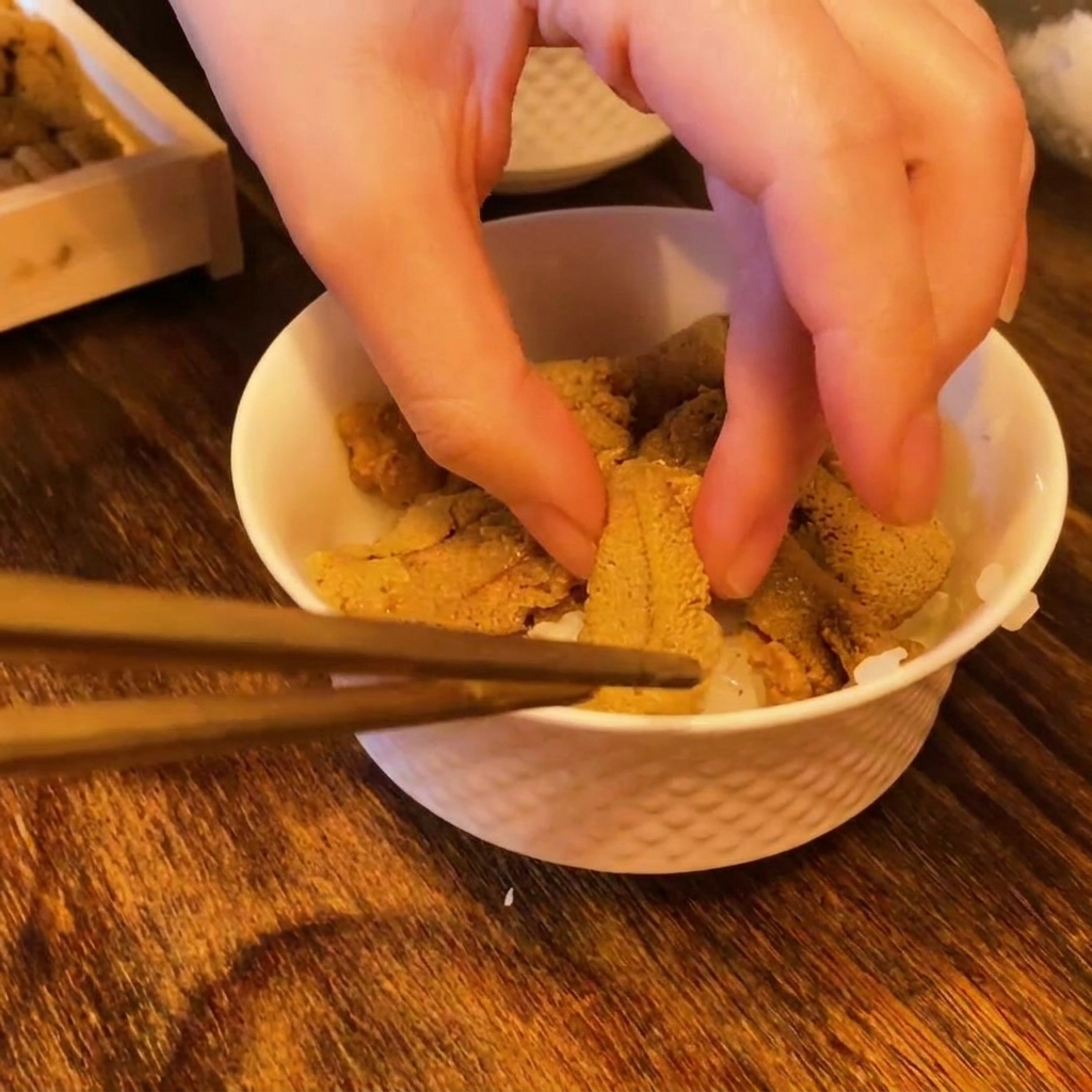 箸を使って、酢飯の上に鮮やかなオレンジ色の生うにを一切れずつ並べている様子。