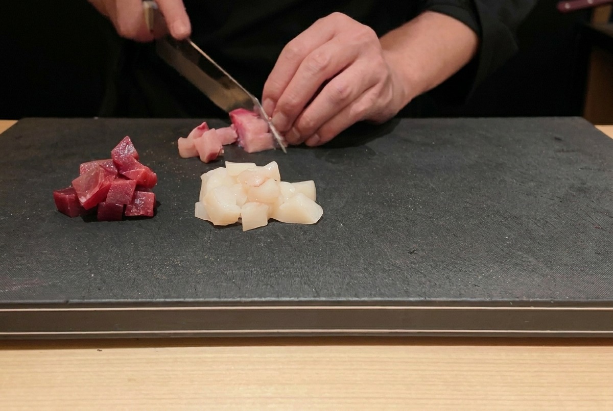 黒いまな板の上で、新鮮なマグロとハマチを小さな角切りにする様子。