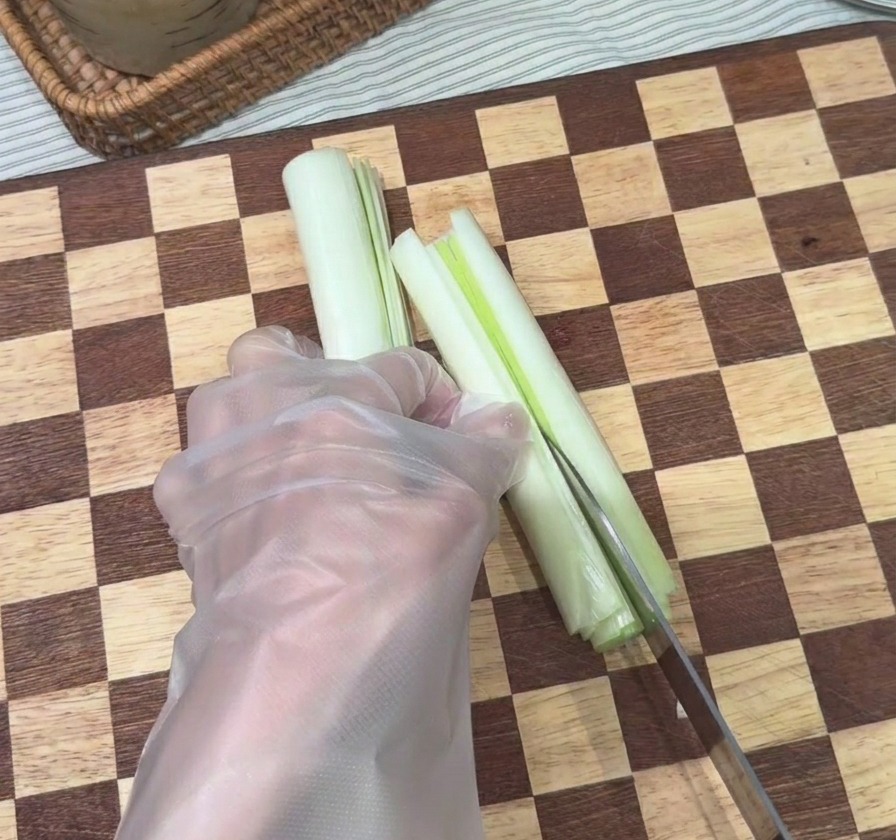 まな板の上で、包丁を使って長ねぎを縦に細く千切りにしている様子。