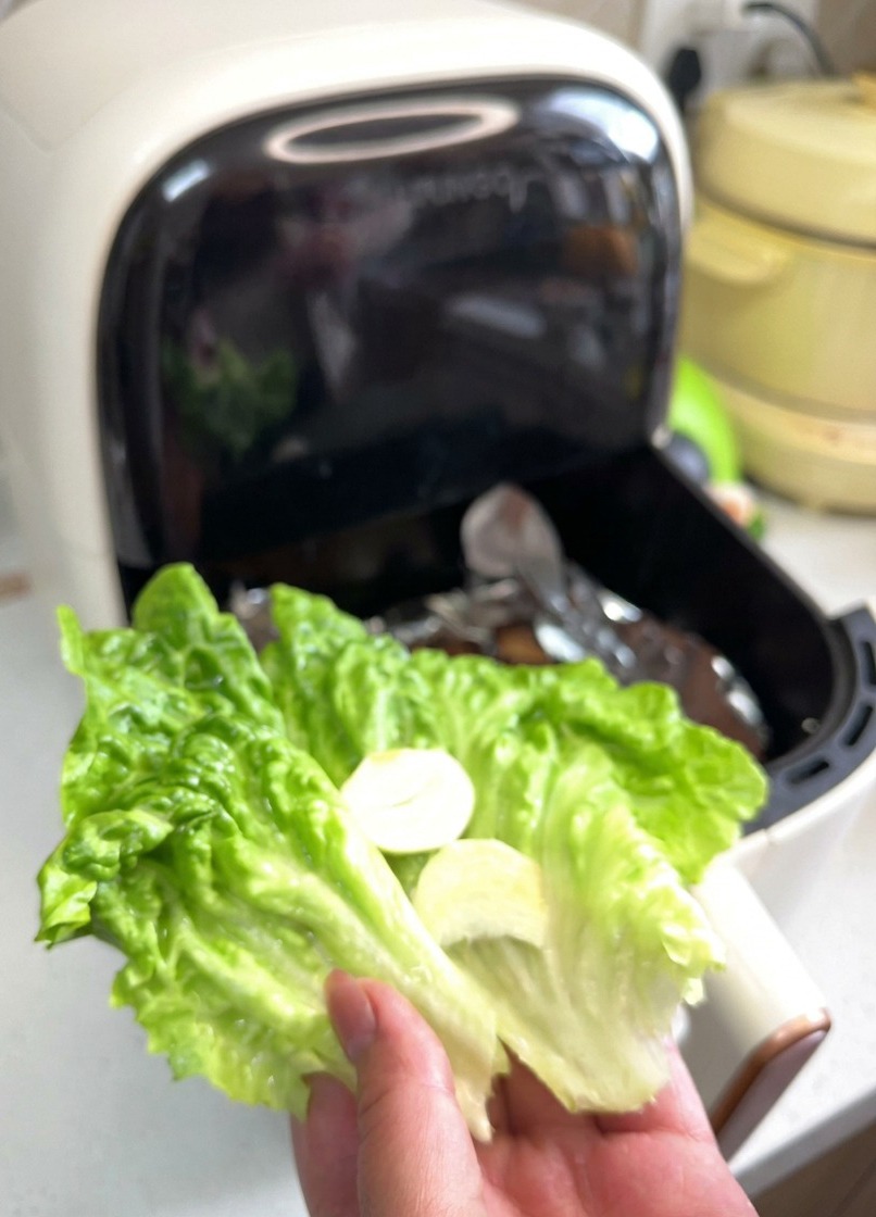 手に持った鮮やかな緑色のレタスの葉の上に、にんにくのスライスと赤玉ねぎの輪切りがのっている様子。