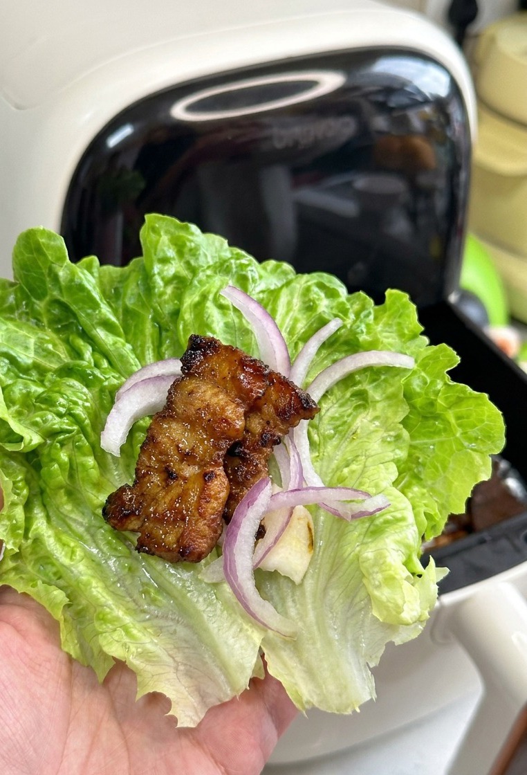 にんにくと玉ねぎが入ったレタスの葉に、程よく焦げ目がついたジューシーな豚バラ肉がのっている様子。