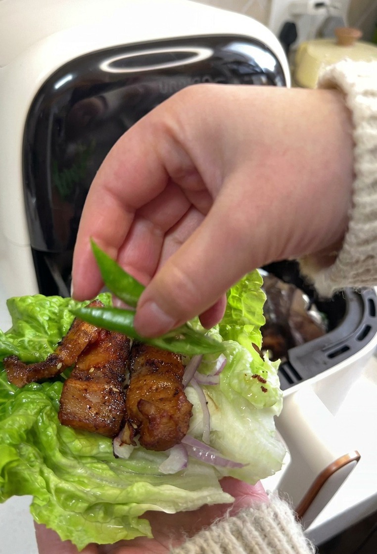 焼いた豚バラ肉と赤玉ねぎがのったレタスの葉の上に、鮮やかな緑色の青唐辛子を2枚添えている様子。