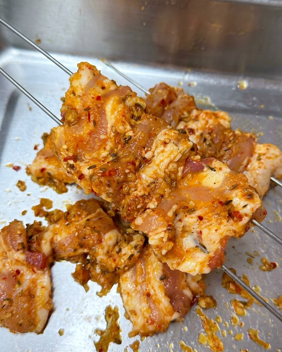 金属製のトレイの上で、マリネした豚バラ肉に2本の細い金串を刺している様子。