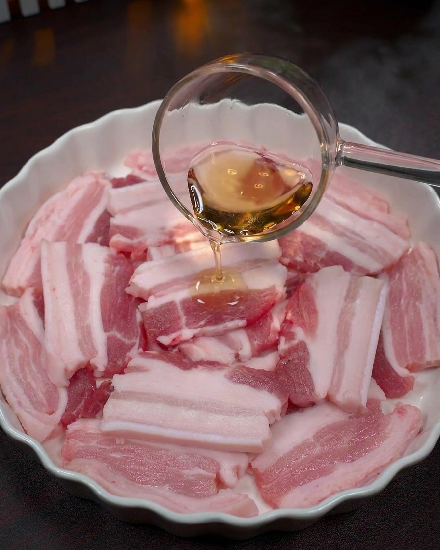 ボウルの中の豚肉に料理酒を注いでいる様子