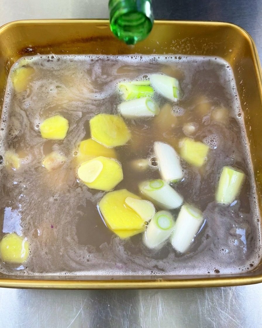 瓶から透明な酒を、生姜やねぎが入ったマリネ液に注ぐ様子。