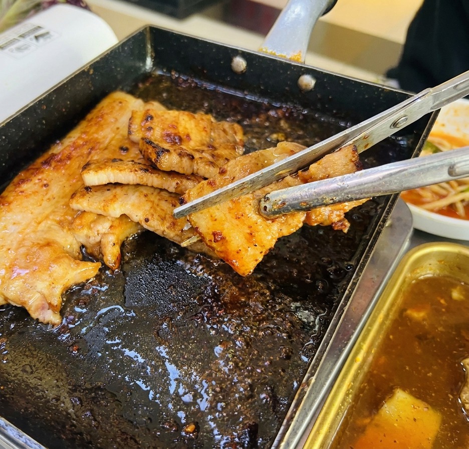 トングとキッチンバサミを使い、焼けた肉を一口大に切っている様子。