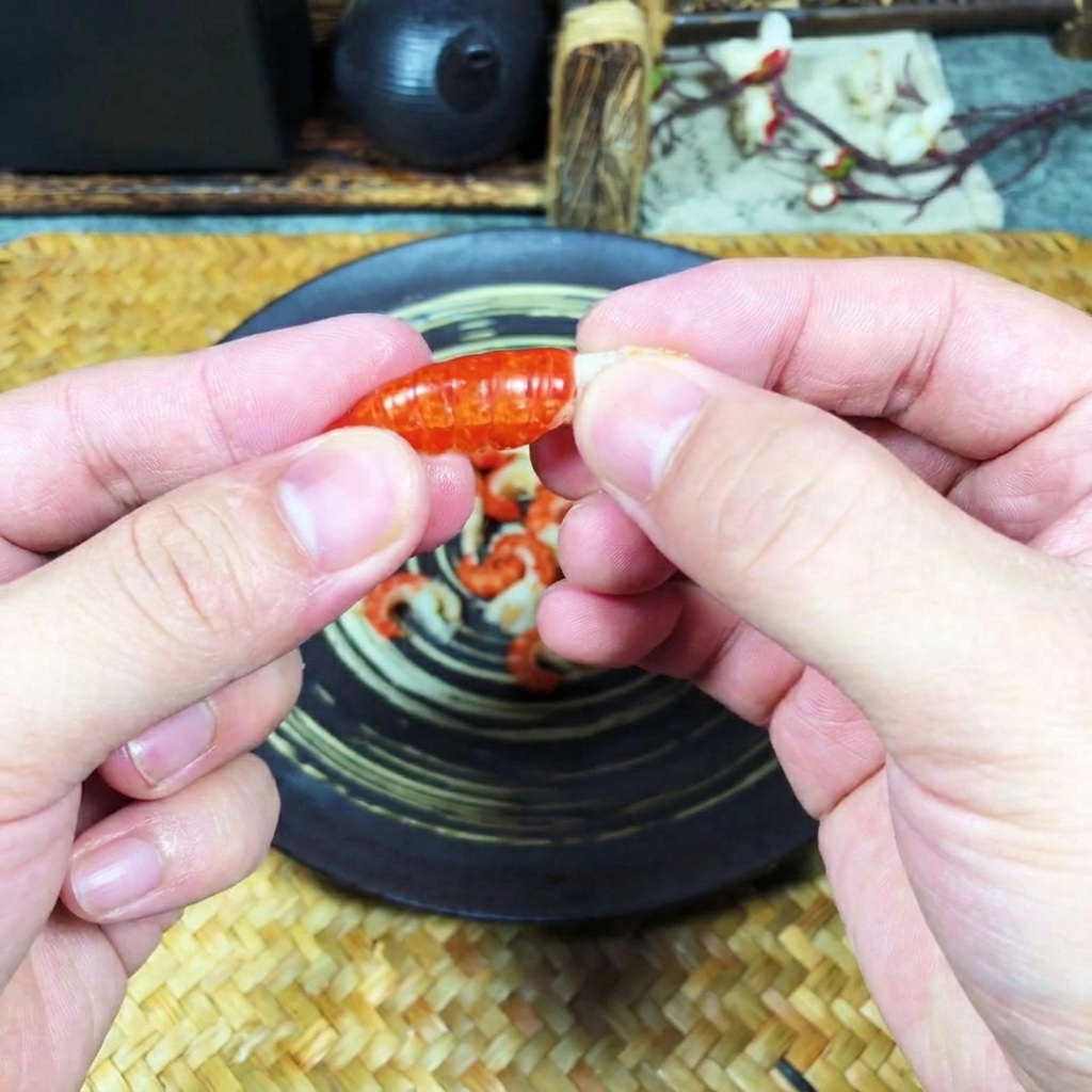 茹でたザリガニのオレンジ色の殻を手でむき、中の白い身を取り出している手元のアップ。