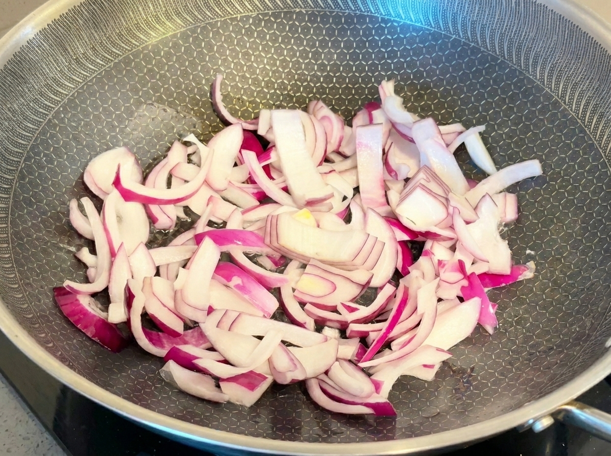フライパンでしんなりするまで炒められている紫玉ねぎのスライス。