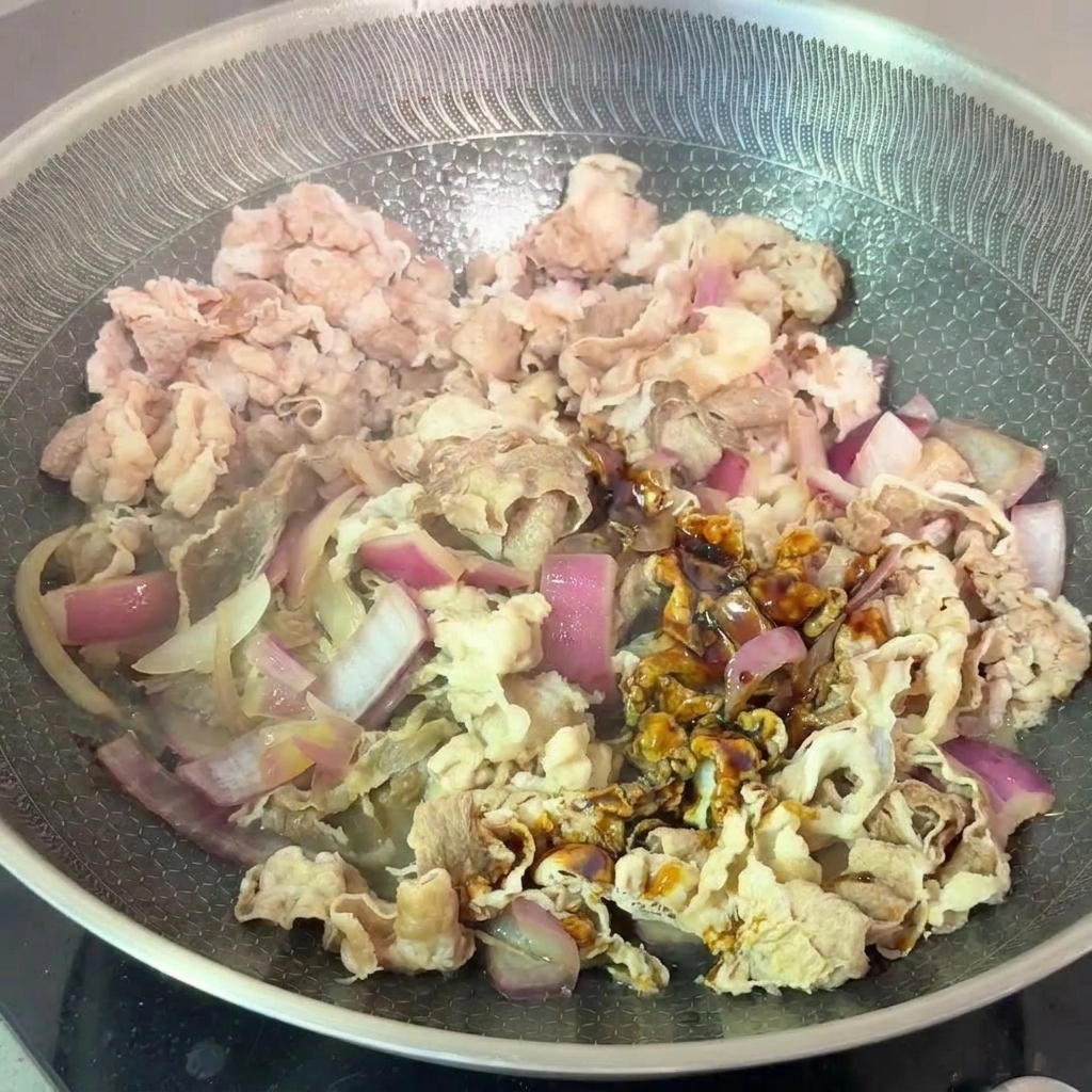 炒めた玉ねぎに下茹でした牛肉と合わせ調味料を加えて混ぜ合わせる様子。