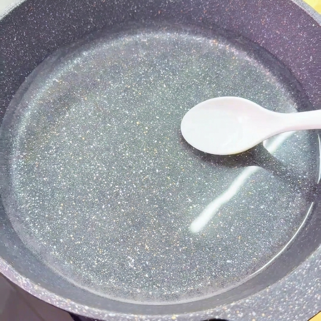 白いスプーンで、透明な冷水が入った中華鍋に塩を振り入れている様子。