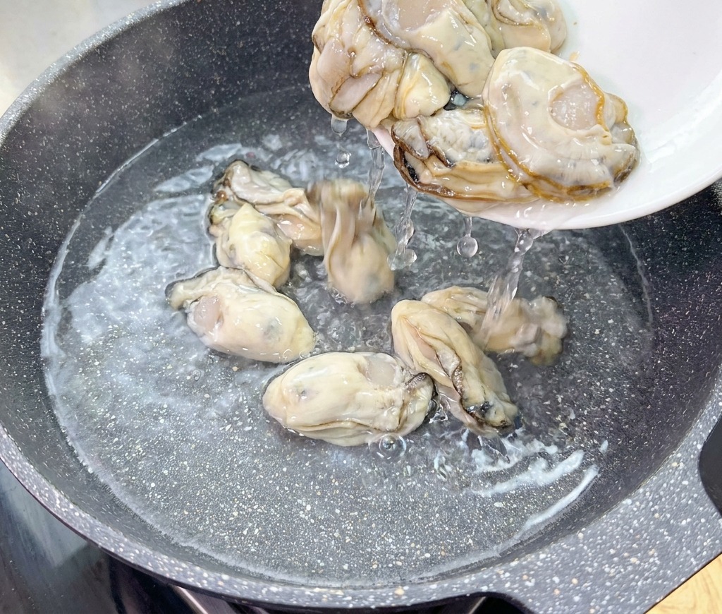 白い皿から、塩を入れた冷水の中華鍋に、新鮮な生の牡蠣を滑らせるように入れている様子。