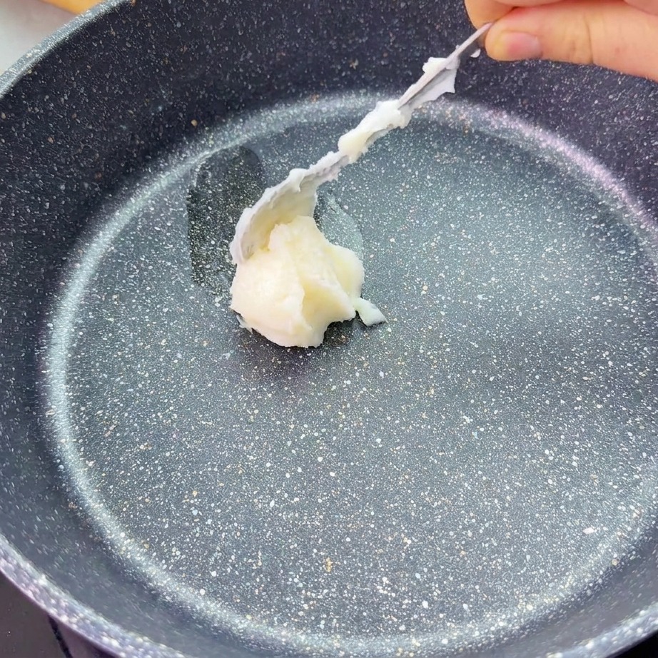 熱したフライパンの中央に、スプーンで白いラードをひとさじ置いている様子。
