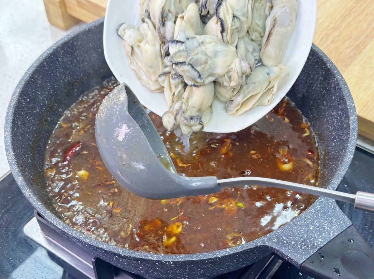 煮立つソースの中に、下茹でして冷やしておいた大粒の牡蠣を皿から投入している様子。