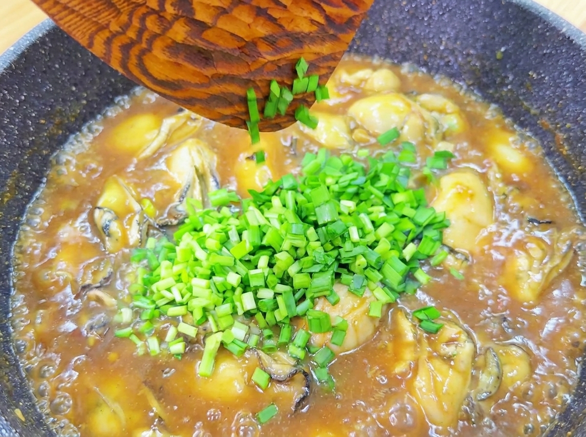 とろみのついた牡蠣のあんかけに、刻みたてのニラをたっぷり散らしている様子。