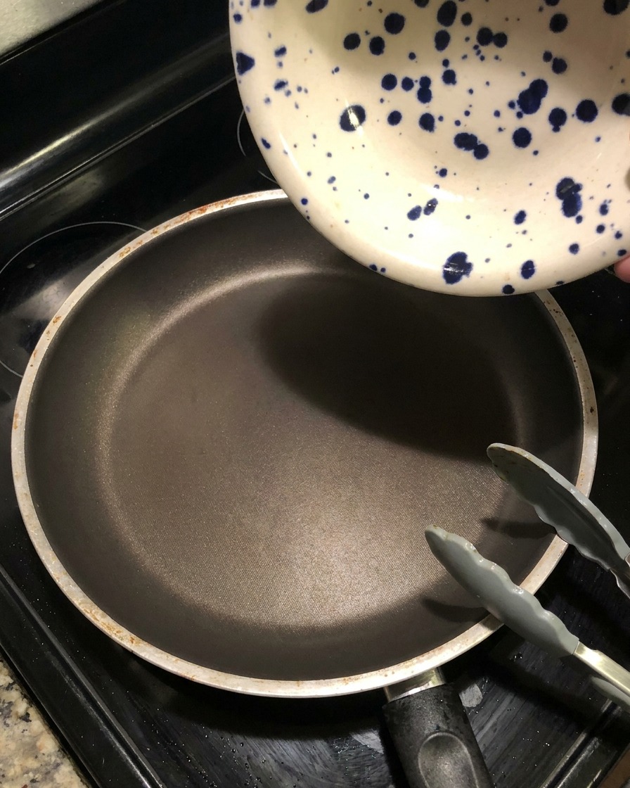 青い模様の入った陶器のボウルから、熱くなった空のフライパンに濃いマリネ液を注ぎ入れ、ソースを煮詰めている様子。