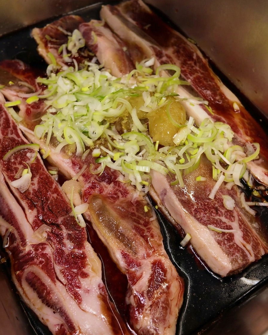 ねぎとにんにくが乗ったリブの上に、艶やかなごま油を回しかけている様子。