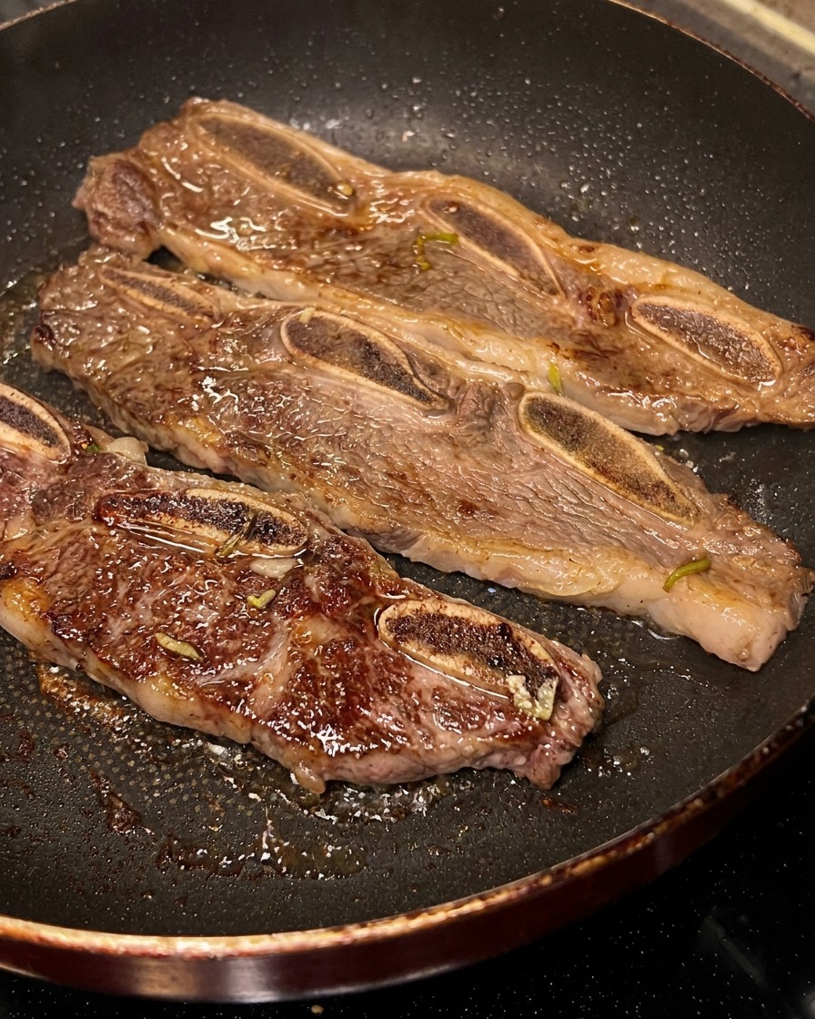 フライパンで焼いているリブをトングで裏返し、こんがりとした焼き色がついている様子。