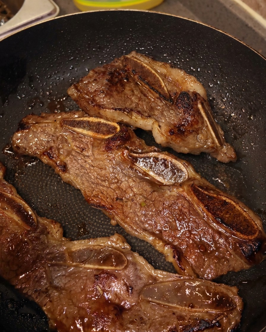 フライパンの中で、キッチンバサミを使って焼けた牛リブを骨ごとに切り分けている様子。