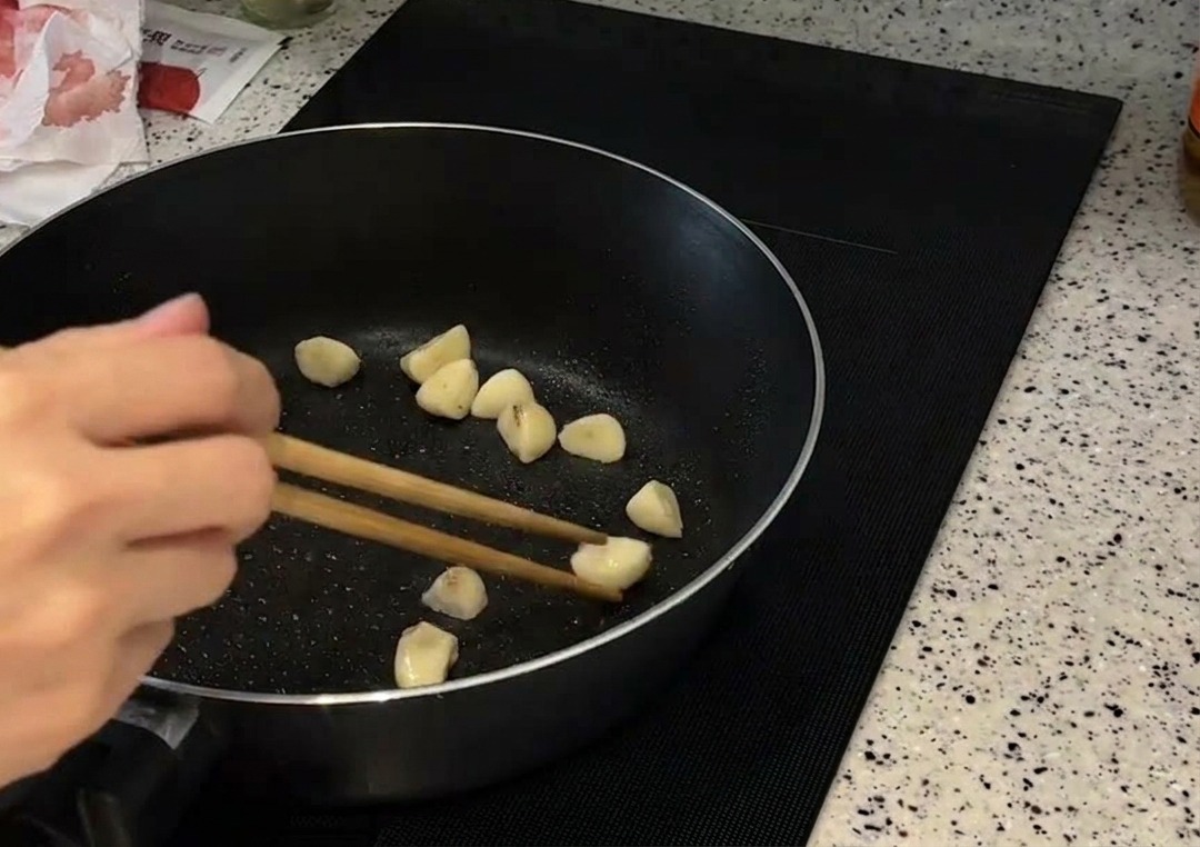 フライパンで丸ごとのにんにくを箸で転がしながら、きつね色になるまで炒めている様子。